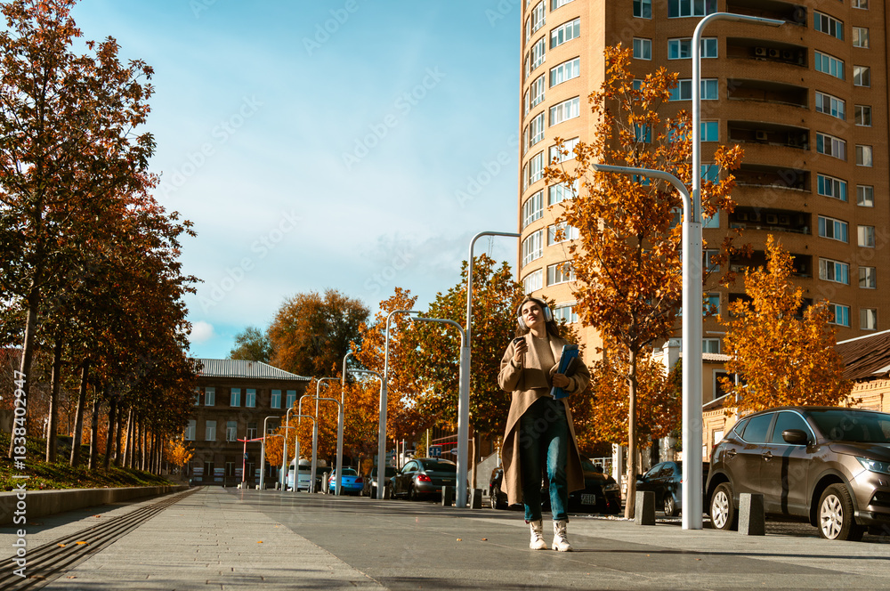 Naklejka premium Woman Walking with Headphones and Coffee in Autumn City