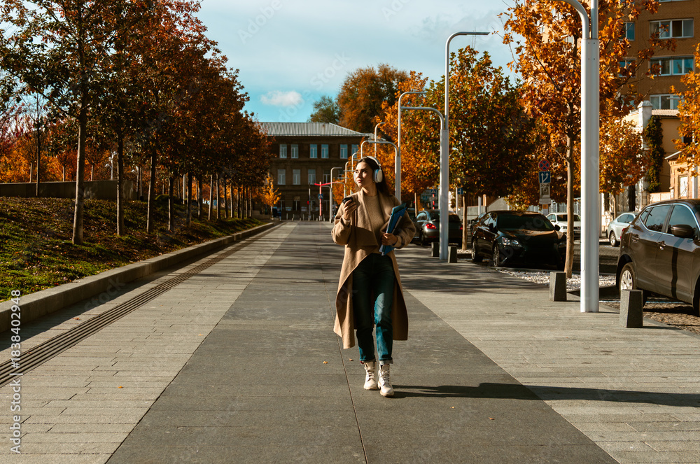 Naklejka premium Woman Walking with Headphones and Coffee in Autumn City