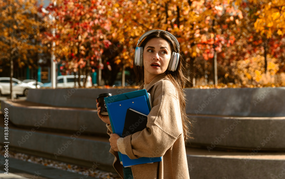 Naklejka premium Woman Walking with Headphones and Coffee in Autumn City