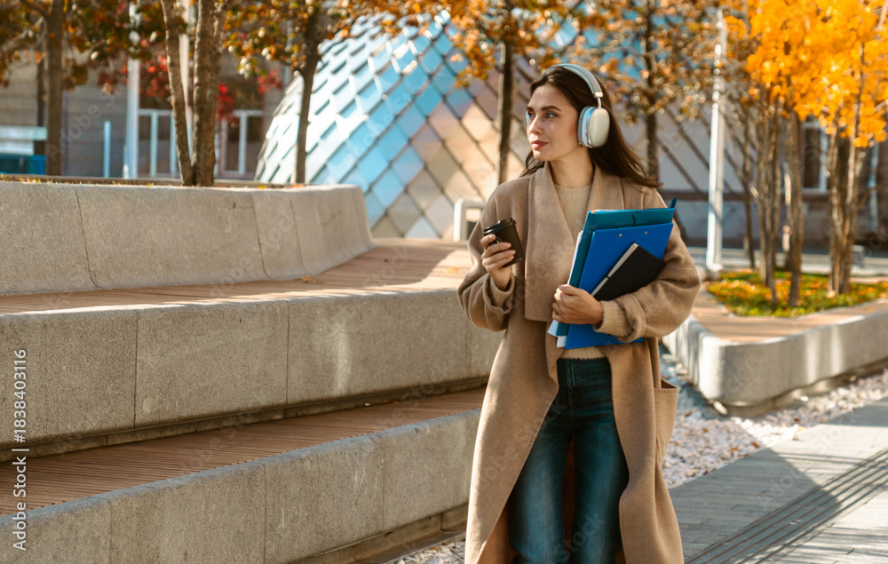 Naklejka premium Woman Walking with Headphones and Coffee in Autumn City