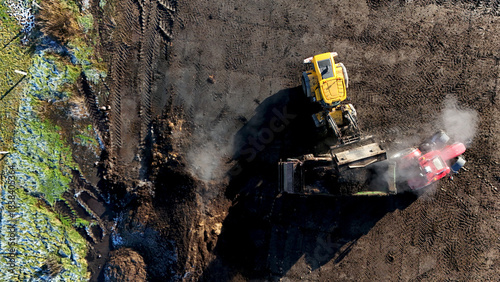Aerial top view of an excavator loading soil into a dump truck during earthworks. Active construction process, heavy machinery operation, industrial textures, and infrastructure development scene.
