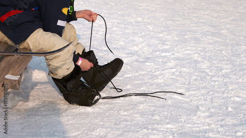A snowboarder lacing his boots outside while sitting on a bench. Detail. Close-up.