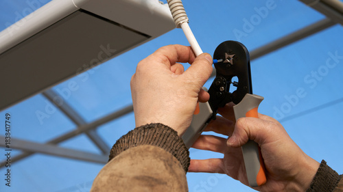 Installing an infrared heater in a greenhouse. Connecting electricity to the heating device. Men's hands crimp the metal end of the wire with a crimper.