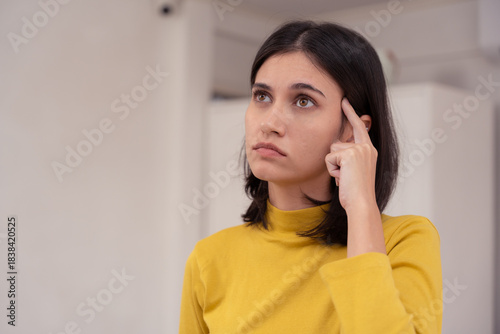 Young woman pointing at her temple and looking confused, indicating memory problems or difficulty concentrating. memory, forget, thinking, mind, brain, confused, confusion, woman, forgetful, problem.