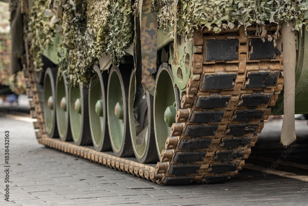 Obraz premium Close-up view of a military tracked tank covered in camouflage netting, showing its heavy armored treads and weathered fabric strips