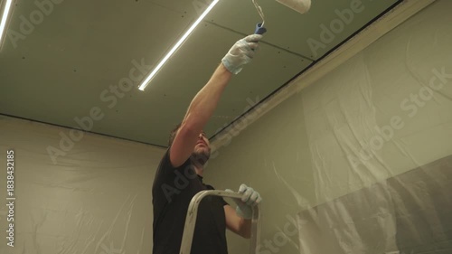 A man primes a drywall ceiling with a roller
