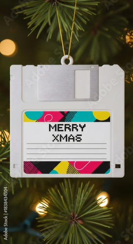 Floppy disk Christmas ornament hanging on a pine branch with decorative lights. Retro 90s aesthetic for holiday seasons and celebration of nostalgia.