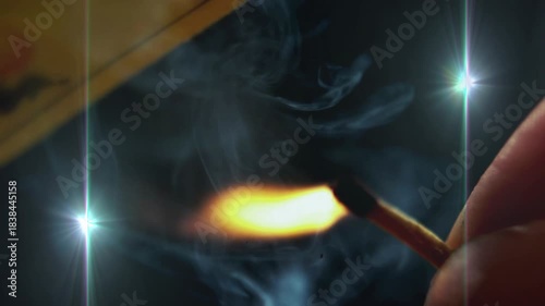 Hand dragging match across striker, match head sparking then igniting, flame growing to light scene