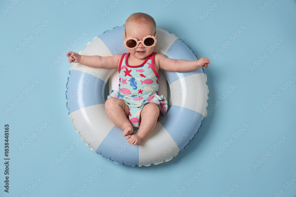 Fototapeta premium Cute little baby with sunglasses on inflatable ring against light blue background, top view