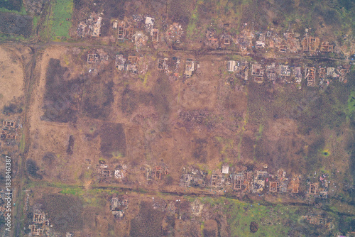 Aerial top down view of destroyed village ruins with roofless foundations. War zone settlement destruction and scorched earth landscape background.