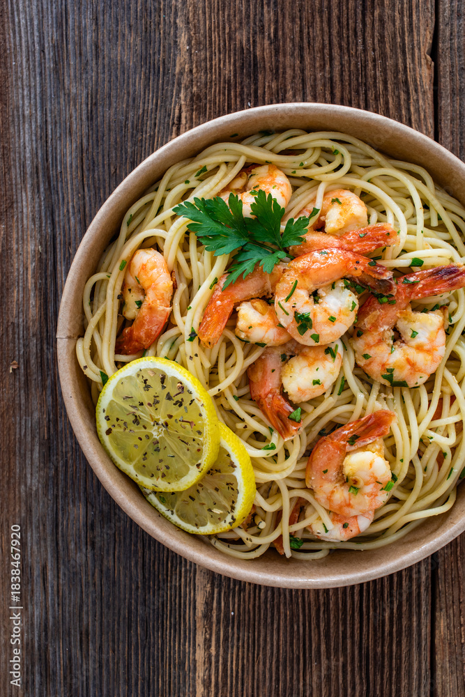 Fototapeta premium Takeaway food - fried shrimps with noodles and lemon in lunch box to go on wooden table