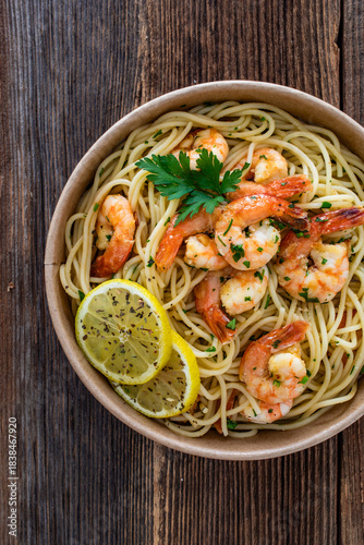Takeaway food - fried shrimps with noodles and lemon in lunch box to go on wooden table
