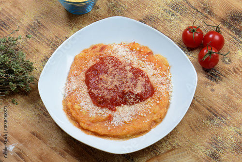 Top view flat lay of traditional Italian polenta with tomato sauce and cheese surrounded by raw ingredients on a wooden table