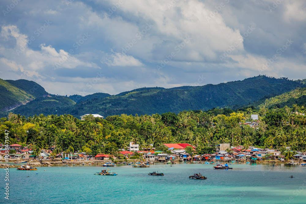 Fototapeta premium Panoramic view of a vibrant coastal community with small fishing boats, tropical vegetation, and rolling hills on a bright tropical day