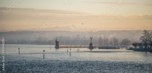 Lake Constance and Constance Harbor with snow-covered Säntis mountain in the background during a pastel-colored winter evening. Konstanz, Baden-Württemberg, Germany.