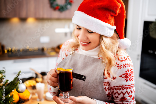 Woman smiling and holding hot mulled wine in christmas and new year kitchen with citrus and spices creating warm holiday atmosphere and cozy winter festive mood