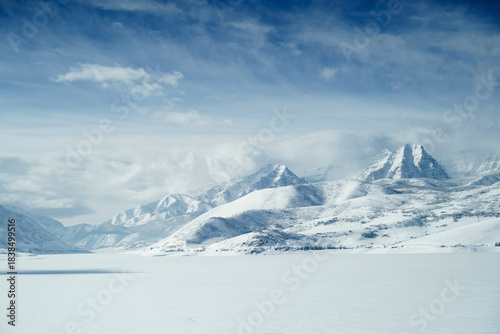 The Wasatch Back Mountains in Heber City Utah over a frozen lake with clouds and snow over mountains and blue sky