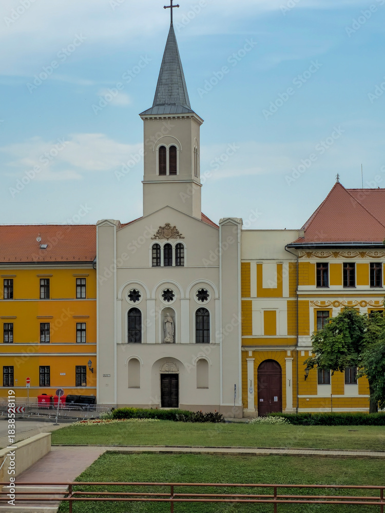 Fototapeta premium Photograph of the Church of Our Lady of the Order of Notre-Dame in Pécs, Hungary. The image shows the church’s architectural details, Gothic and Baroque elements, and surrounding environment. Ideal fo