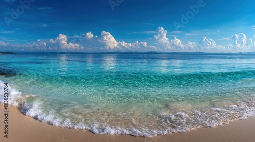 Soft waves lap against the shore revealing fine sand and bright sunlight. The water is clear and blue reflecting clouds in the sky. This location captures a vibrant beach moment.
