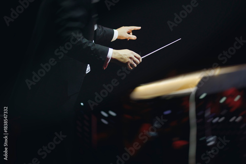 Male conductor behind the podium directing orchestra on stage with pupitre, musicians and choir, the philharmonic venue hall during concert, symphony orchestra director hands conducting waving baton