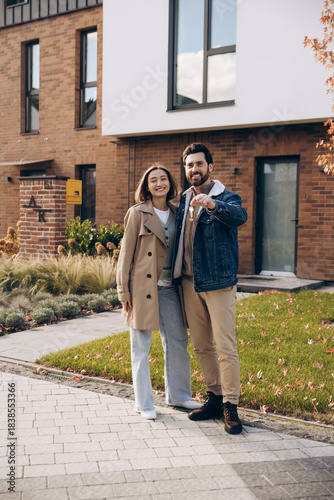 Fotografie Happy smiling couple holding house keys standing in front of new home
