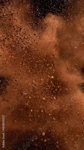 Dramatic high speed capture of rich brown powder exploding outwards creating a striking abstract shape against a deep black background