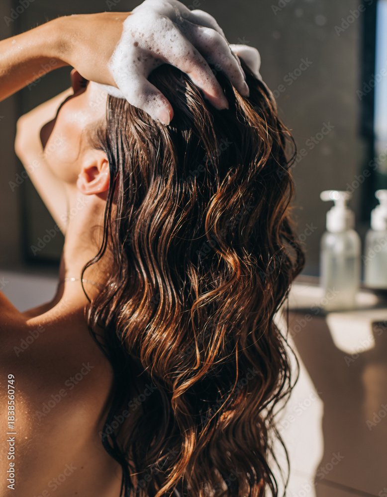 Naklejka premium Woman washing her hair with shampoo, closeup. Focus on wellness, selfcare and beauty. Represents hygiene, cleanliness, healthy lifestyle, routine, and relaxing moments.
