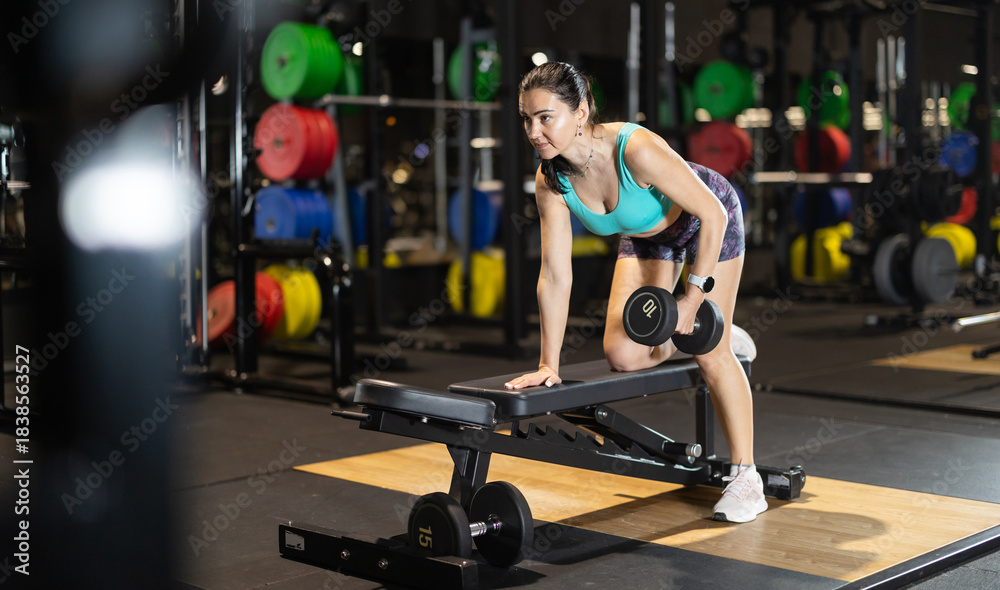 Fototapeta premium Woman trains muscles of arms, perform exercises with dumbbell. Energetic sport club client during grueling workout