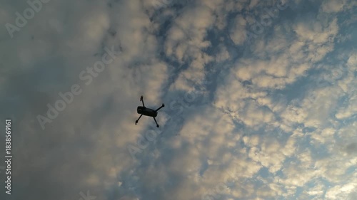 Drone hovers, rotates, then flies sideways to right under sky and clouds