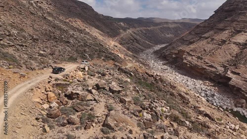 Aerial view of driving cars in dry valley in the island of Socotra. Motion drone video of moving cars on bumpy road surrounded by stones and dessert plants. Following cars from the air. Off-road drive