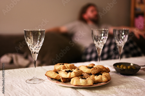 A warm, intimate indoor scene featuring crystal wine glasses and a plate of homemade puff-pastry cookies