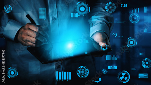 Photos A person interacts with a tablet surrounded by a glowing digital interface, symbolizing modern technology and data analysis in a sleek workspace environment