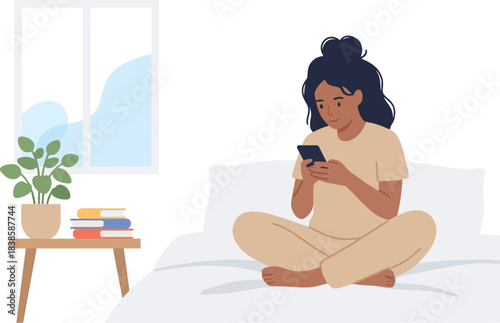Casual young woman sitting cross-legged on bed using smartphone in cozy bedroom with window and potted plant minimalist style