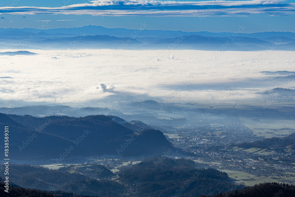 Obraz premium A panoramic view from the high plateau shows surrounding mountain ranges and a valley densely covered in a thick layer of inversion fog