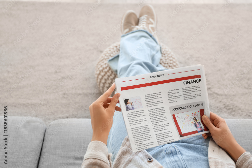 Naklejka premium Young woman with newspaper sitting on sofa at home, top view
