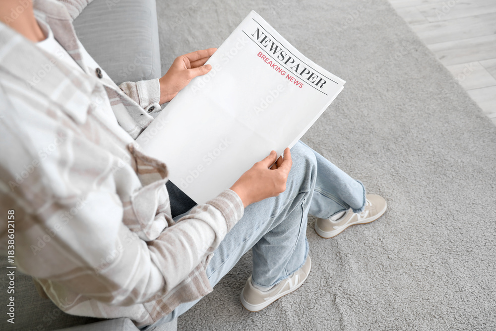 Fototapeta premium Young woman with blank newspaper sitting on sofa at home