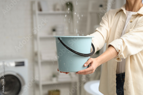 Foto Young woman placing bucket under water dripping from ceiling in bathroom, closeu