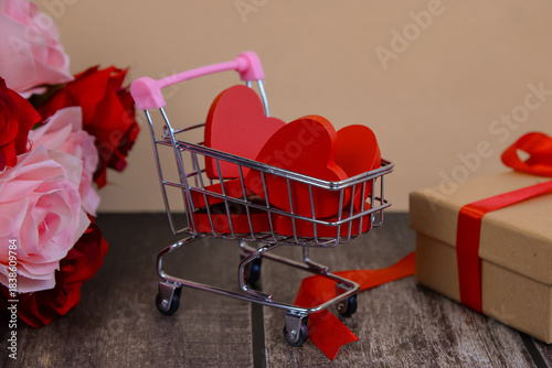 Hearts in shopping cart and supermarket trolley against colored background.