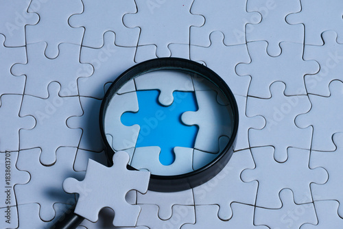 Magnifying glass focusing on the missing gap of a white puzzle, with the missing piece placed on the magnifying glass, representing problem solving, gap analysis, and root cause analysis