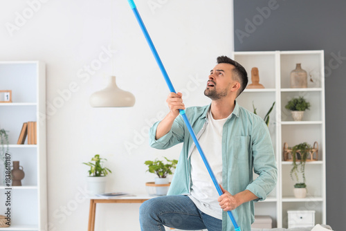 Foto Young man banging ceiling with mop because of loud neighbours at home