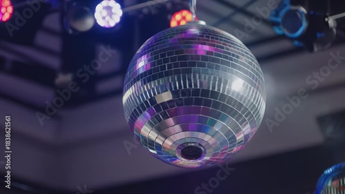 A shiny disco ball hangs from the ceiling, reflecting vibrant purple and pink lights in a dimly lit club or party venue.