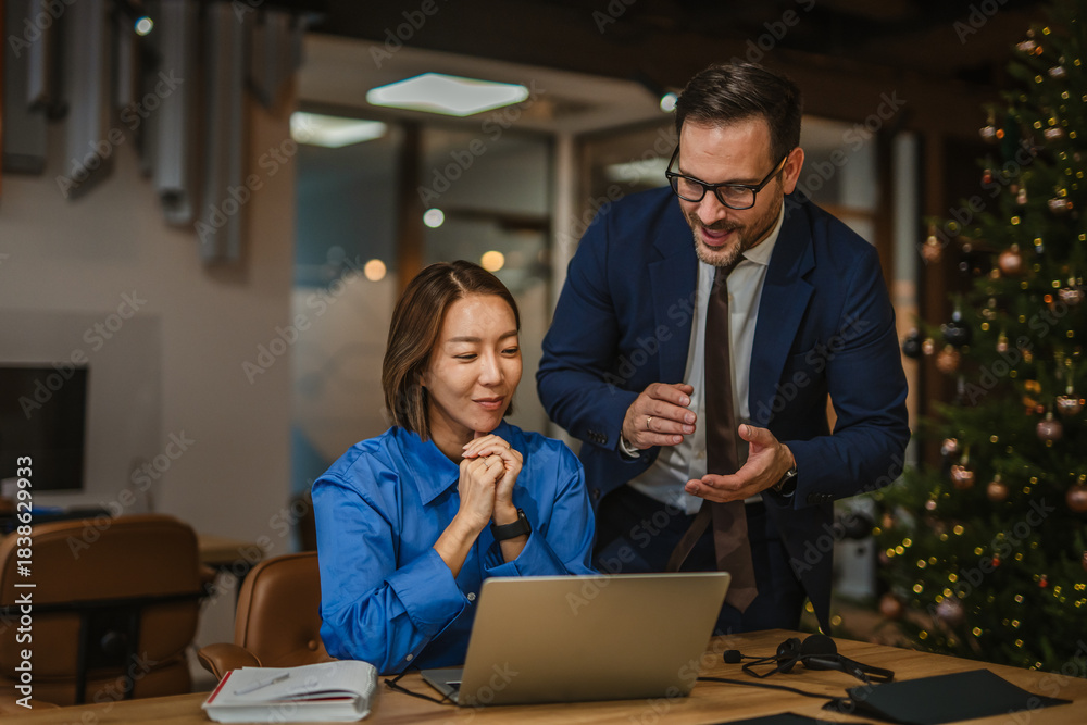 Fototapeta premium Diverse business colleagues collaborating on laptop in a festive office