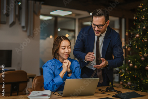 Diverse business colleagues collaborating on laptop in a festive office