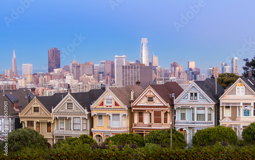 Iconic Painted Ladies overlooking San Francisco skyline with pastel Victorian architecture lush greenery foreground twilight urban backdrop shimmering towers historic charm vibrant cityscape