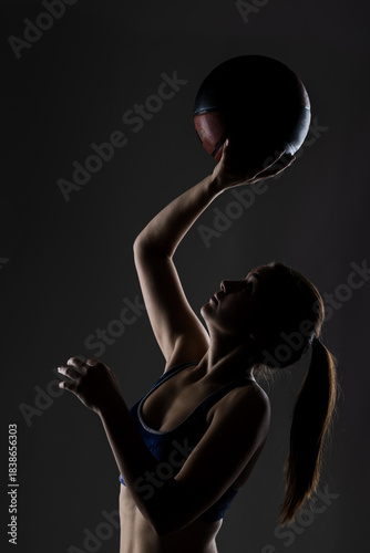 Athletic young woman in sports attire posing with a basketball, highlighting her silhouette and physique