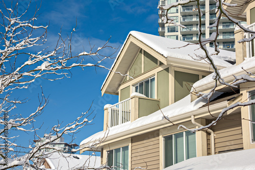 Top of residential house in snow and high-rise building on blue sky background