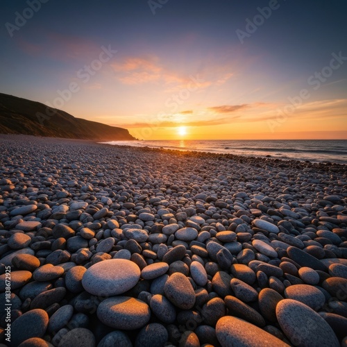Coastal sunrise over a pebble beach with hills in the background; warm, golden tones