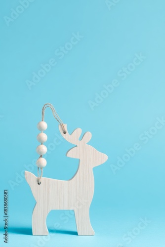 A vertical shot of a deer-shaped wooden Christmas ornament isolated on a blue...