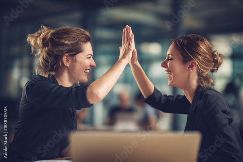 Celebrating success two women high-fiving at desk in modern office environment