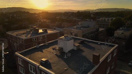 Golden hour aerial view of residential and commercial buildings bathed in warm sunlight, overlooking a peaceful urban landscape with distant mountains at sunset